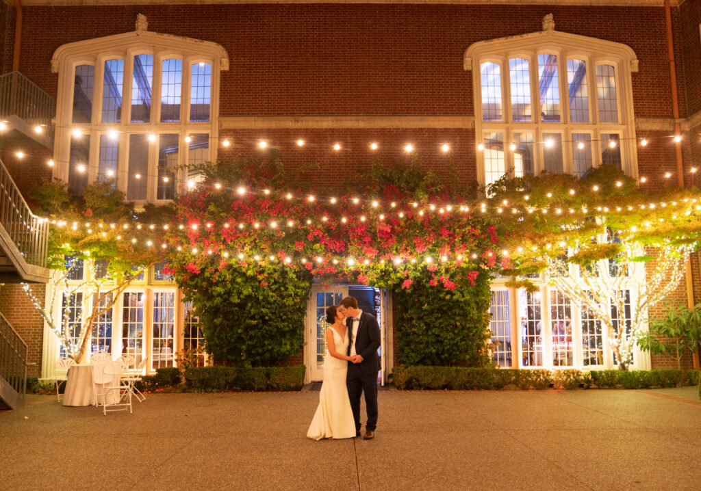 Newlyweds posing by wedding venue with warm evening lights