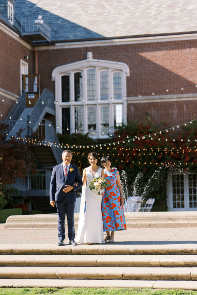 Bride posing with parents outdoors in wedding attire