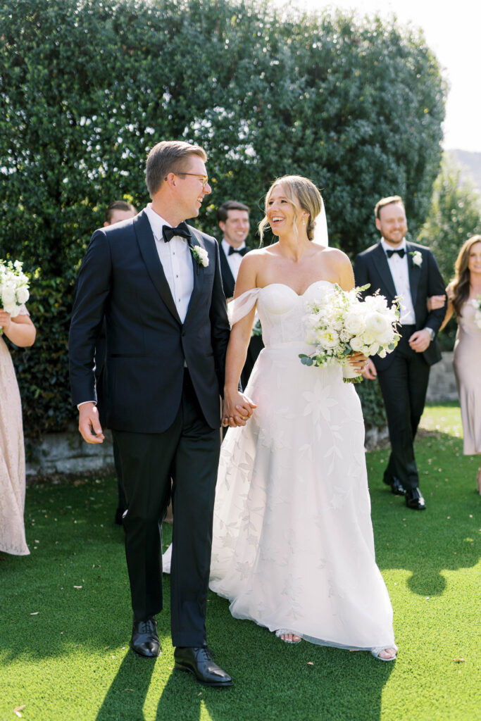 bride and groom holding hands while smiling at each other