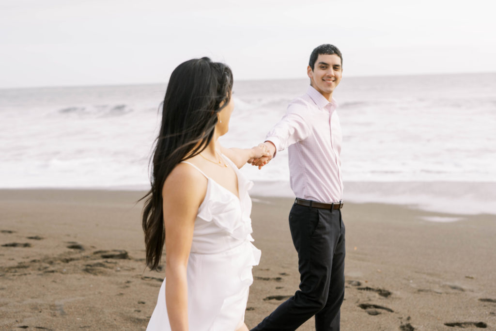 bride and groom walking on the beach while holding hands