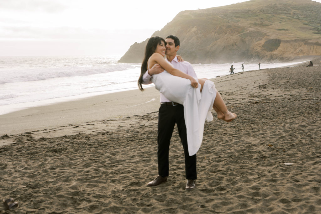 groom holding bride in his arms at the beach