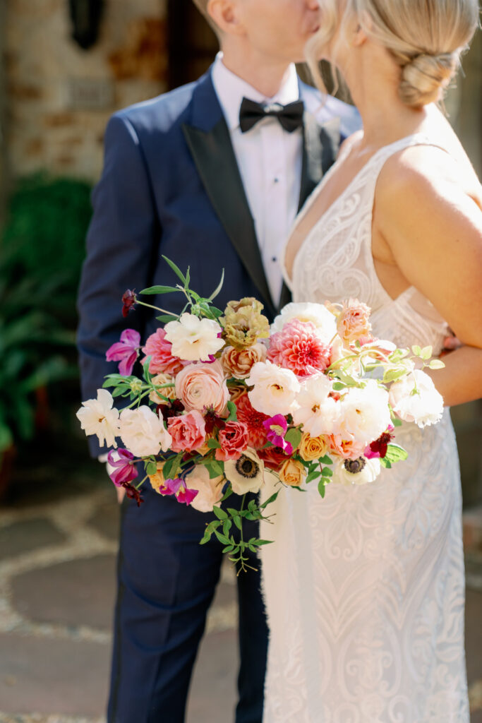 close up photo of bride bouquet with bride and groom in the background