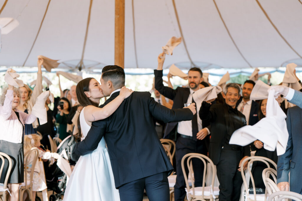 guests hyping up bride and groom kissing at the reception