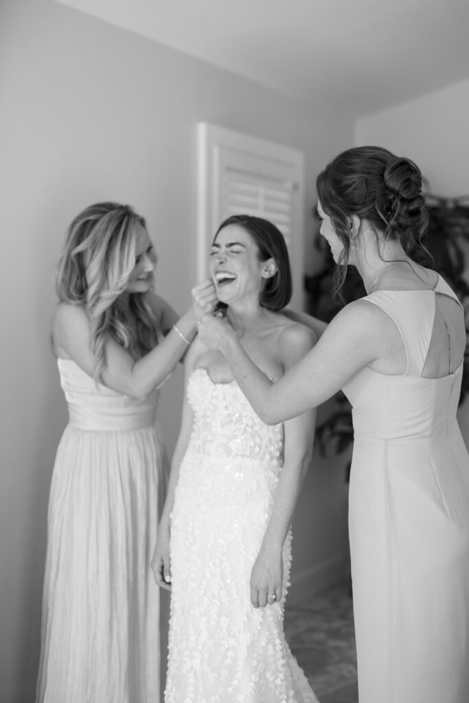 bride laughing as bridesmaids help her get ready