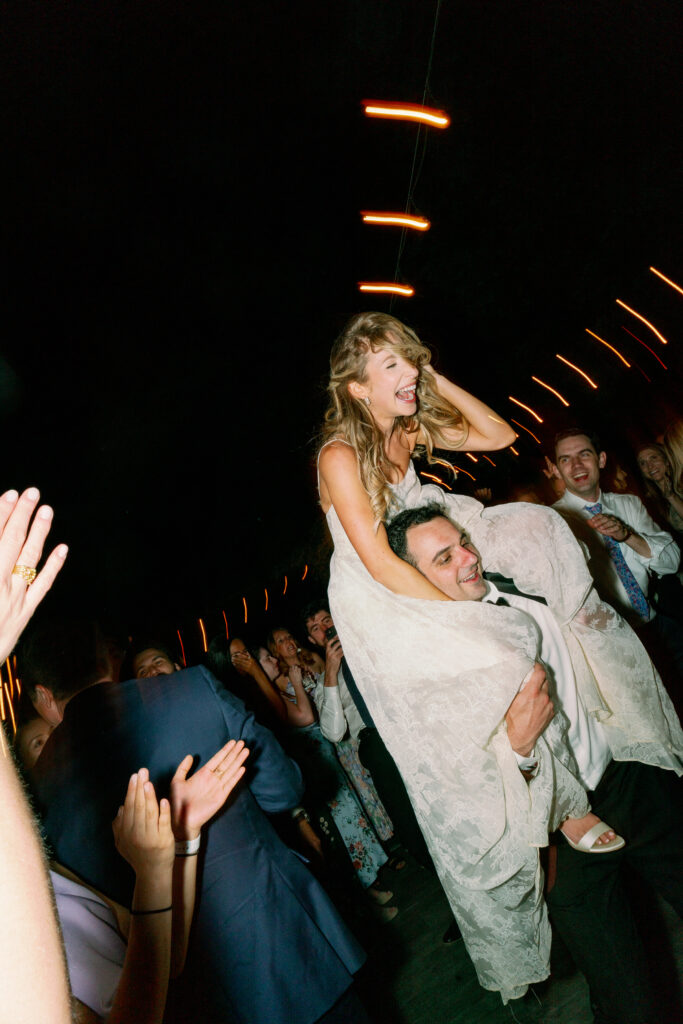 bride being carried over groom's shoulder at the dance floor