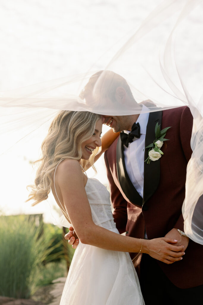 bride and groom smiling while under the bride's veil